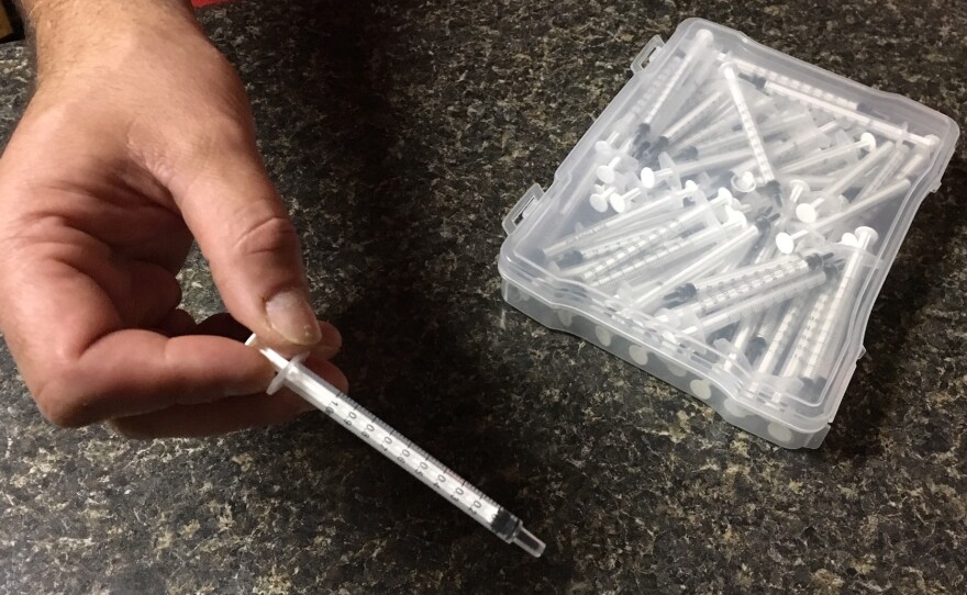 Chris holds a plastic syringe he and his wife use to administer homemade medical marijuana oil to their 13-year-old son, Dylan, who has autism.