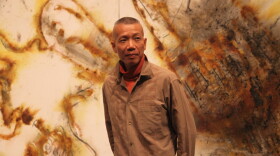 Artist Cai Guo-Qiang stands in front of a gunpowder drawing, <em>Desire for Zero Gravity</em>, at The Museum of Contemporary Art in Los Angeles. Cai uses a pyrotechnic process to burn shapes into large-scale canvases.<em></em>