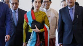 In this photo provided by the Myanmar State Counsellor Office, Aung San Suu Kyi, center, departs from Naypyitaw International Airport in Naypyitaw, Myanmar on Sunday.
