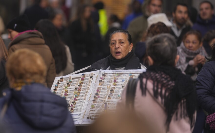 A Christmas lottery seller looks for customers in a crowded street in Madrid, Spain, Sunday, Dec. 3, 2023. (AP Photo/Paul White)