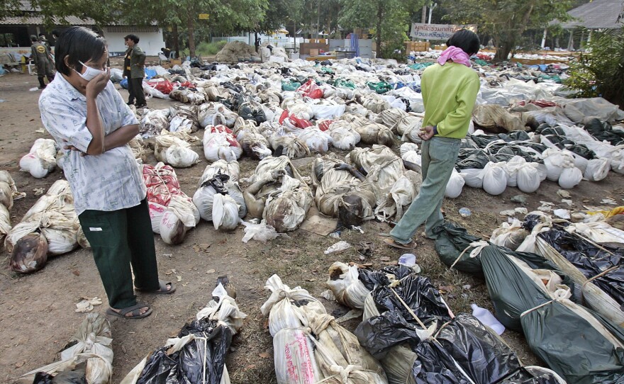 In a Dec. 30, 2004 file photo, Thais walk outside a Buddhist temple, near Takuapa, Thailand, where more than 1,000 bodies had been gathered.