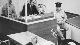 Defendant Adolf Eichmann takes  notes during his trial in Jerusalem.  The glass booth in which Eichmann sat was  erected to protect him from assassination.