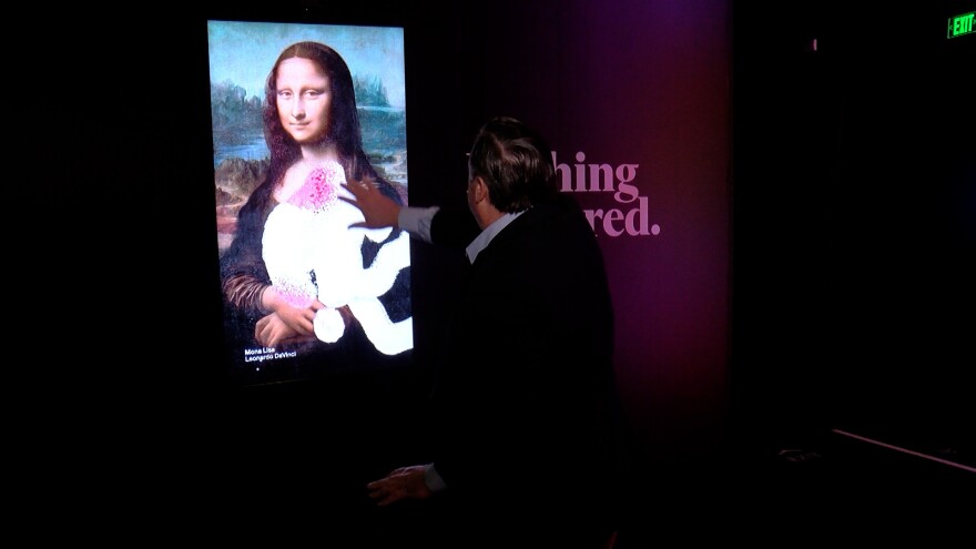 KPBS reporter John Carroll is shown in front of an interactive screen featuring works of well known art on January 17, 2023.