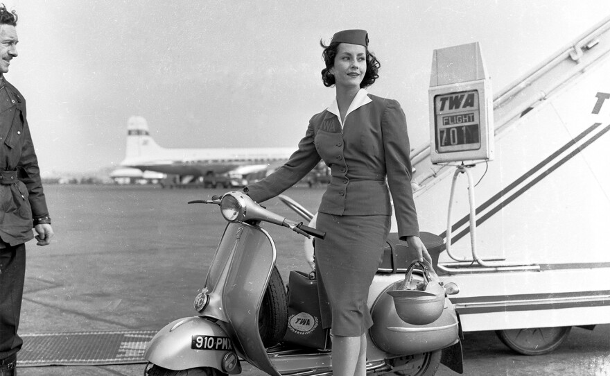 TWA stewardess stands on tarmac, 1955.