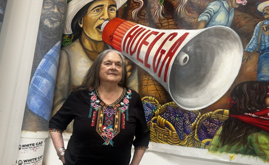 Muralist and activist Judy Baca stands in front of a section of The Great Wall of Los Angeles that is still being reconsidered. Cesar Chavez's image is rolled up and hidden for now, next to the depiction of Dolores Huerta.