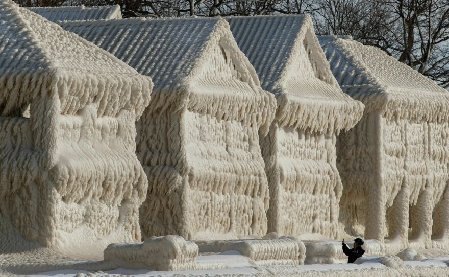 A person takes photos of a scene of frozen houses in the waterfront community of Crystal Beach in Fort Erie, Ontario, Canada.