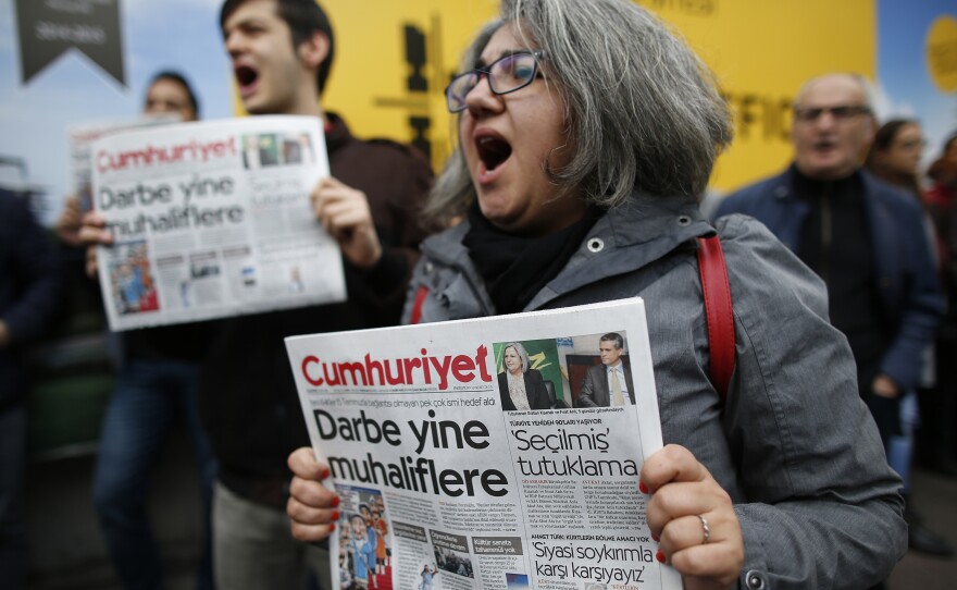 Readers shout slogans as they hold the latest copy of Cumhuriyet in Istanbul. The BBC says the headline reads: "Coup against opposition."