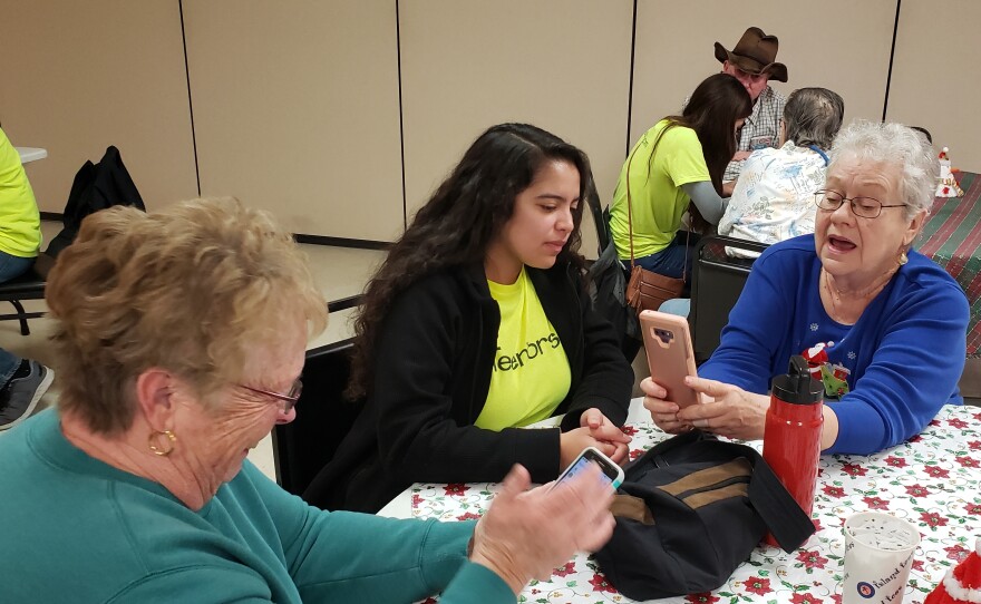 Kendra Gonzales coaches Linda Haverty on how to add a photo of a friend to her contacts list on her phone.