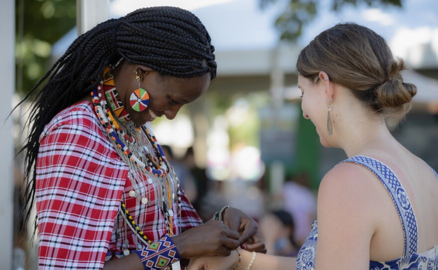 Simaloi Saitoti, a Maasai bead artist from Kenya, ties a bracelet around a visitor's wrist. Saitoti is one of many artisans around the world showcasing their works at the Smithsonian Folklife Festival.