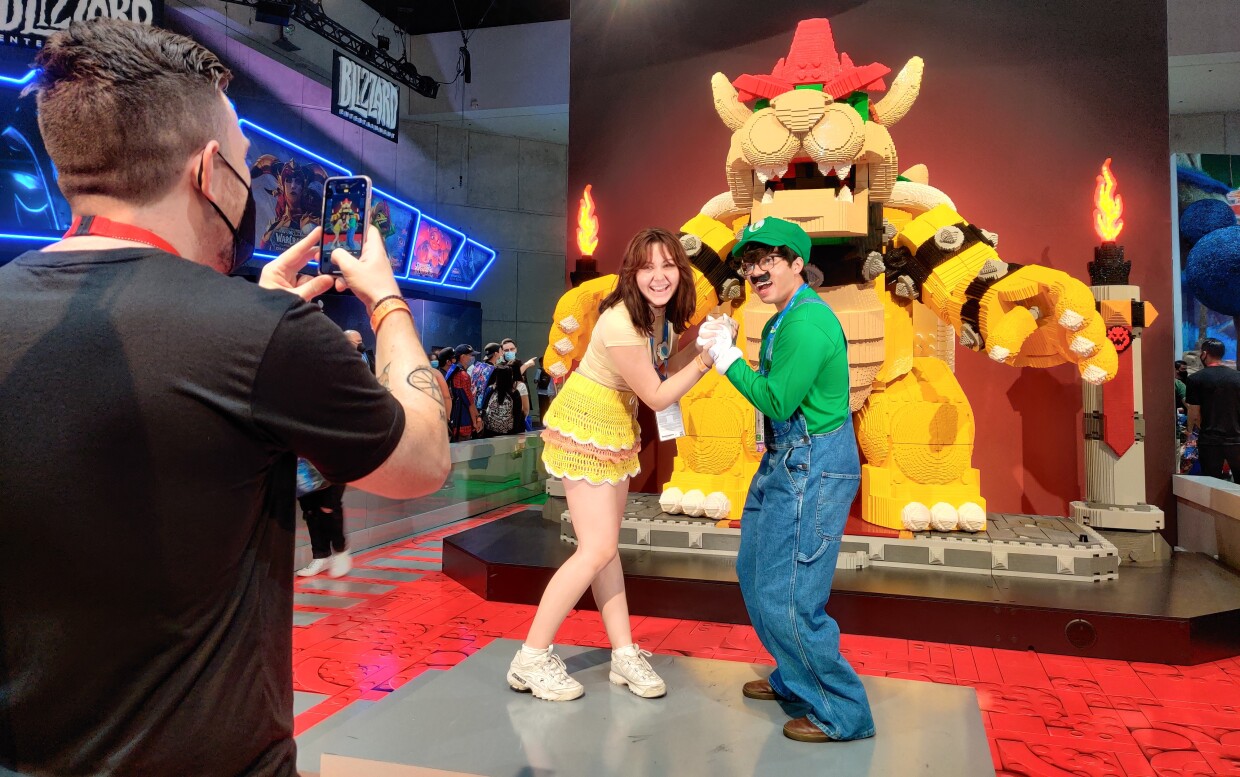 Sarah Maldrett (Daisy) and Luke Vore (Luigi) pose for a photo with a giant Bowser at the LEGO booth in Comic-Con's Exhibit Hall, July 24, 2022.