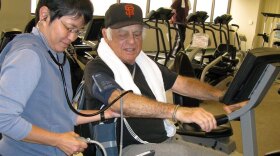Actor Jonathan Haze bicycles at the Cardiac Rehab Lab at Cedars-Sinai Heart Institute.  Exercise physiologist Asako Oshiro takes his blood pressure while he’s pumping.