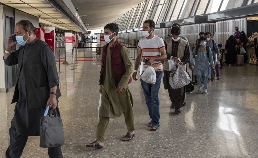 Refugees from Afghanistan are escorted to a waiting bus after arriving and being processed at Dulles International Airport in  Virginia on Monday. The federal government is reportedly offering COVID-19 vaccines for Afghan arrivals at a site near the airport.