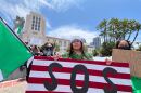 Karina Avila (center) holds an upside down American flag with the letters "SOS" on it at the "No Kings" Day protest in downtown San Diego on June 14, 2025. "No Kings" Day is part of a nationwide demonstration against the policies of the Trump administration. 