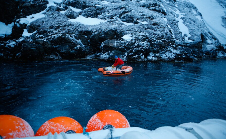 A visitor rows an inflatable dinghy loaded with fresh water to a small dock at the old settlement of Kangeq, Greenland. The village was officially shut down by the Danish government in the 1970s, and its residents were moved to a concrete apartment block in the capital city.