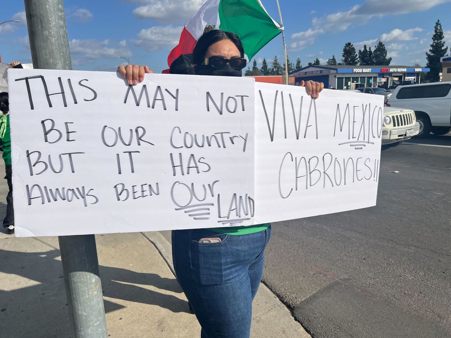 A demonstrator holds signs that reads "This may not be our country, but it has always been our land," and "Viva Mexico c-------" at a protest on Washington Avenue and Escondido Boulevard in Escondido on Jan. 29, 2025.