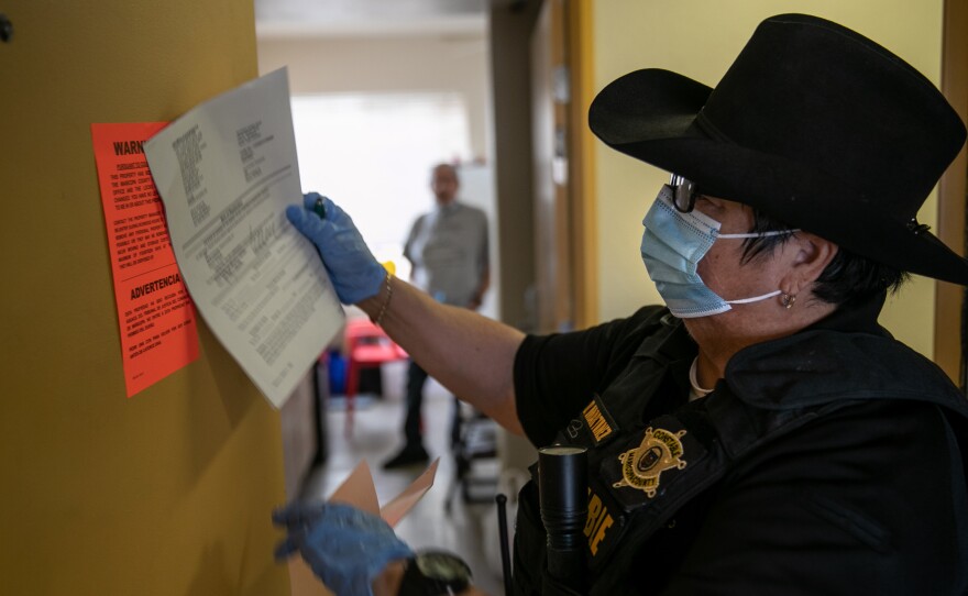 A Maricopa County constable posts an eviction order for non-payment of rent in October in Phoenix, Arizona. The Centers for Disease Control (CDC) is extending an order aimed at preventing evictions. That should protect many people, but thousands of court-ordered evictions continue nationwide due to loopholes in the CDC moratorium.