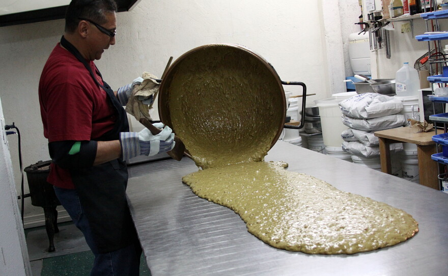Luis Flores, owner of Las Cruces Candy Company, pours hot green chile pecan brittle on a table for cooling. 