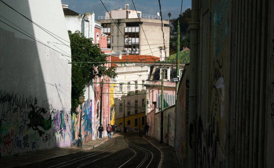 People walk on a steep street next to tracks for the Elevador da Glória in Lisbon, Portugal.