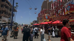 Visitors walk down a food-vendor lined walkway as the gondola ride passes overhead at the San Diego County Fair on June 10, 2026.