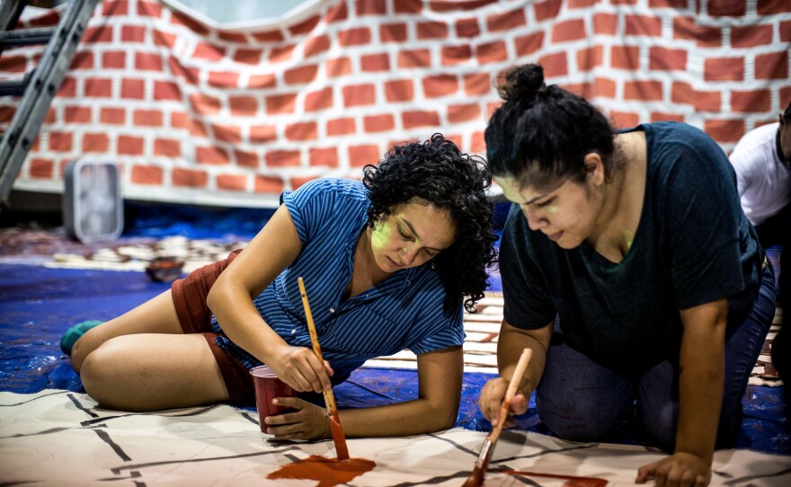 Marisa Franco (left), an organizer with Mijente, and another volunteer paint a portion of "wall" for the protest.