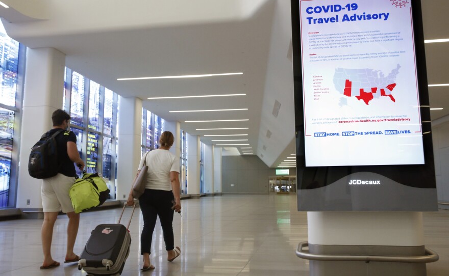 Arriving travelers walk by a COVID-19 travel advisory sign in the baggage claim area at New York City's LaGuardia Airport. New York state is requiring travelers from states on its quarantine list to show proof that they've completed a form with their contact information.