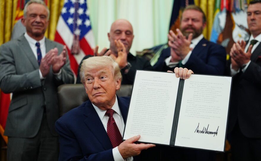 President Donald Trump holds up a signed executive order in the Oval Office of the White House on Saturday in Washington.