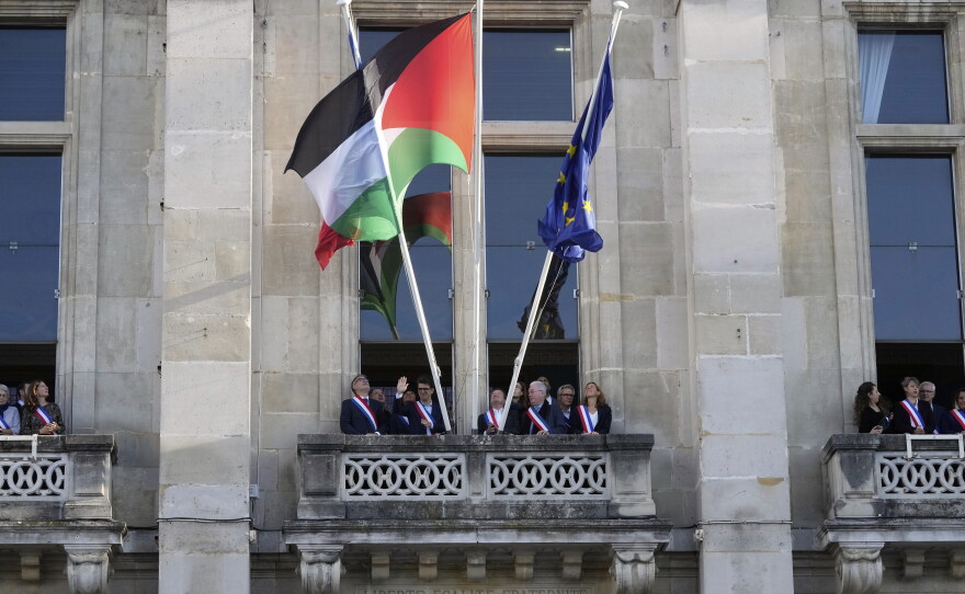 Officials wave after the Palestinian flag (center) has been set on the facade of the Saint-Denis city hall, outside Paris, Monday. France is helping organize efforts toward reviving a two-state solution to the Israeli-Palestinian conflict.
