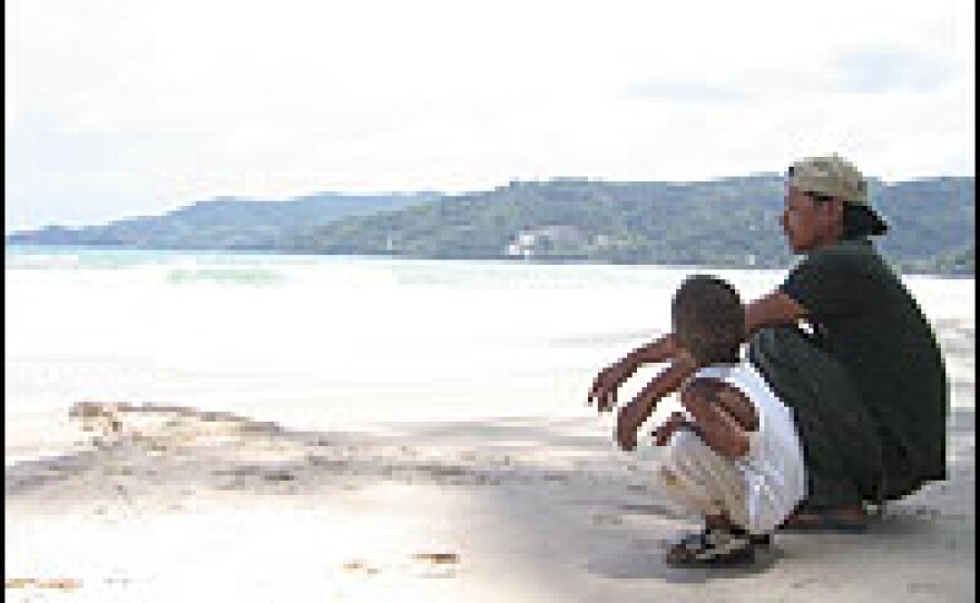 A Thai father talks to his son at Patong Beach in Phuket, Thailand. While locals who rely on tourist income are struggling, the government must decide how to spend money: on tourism development or the immediate needs of local businessmen.