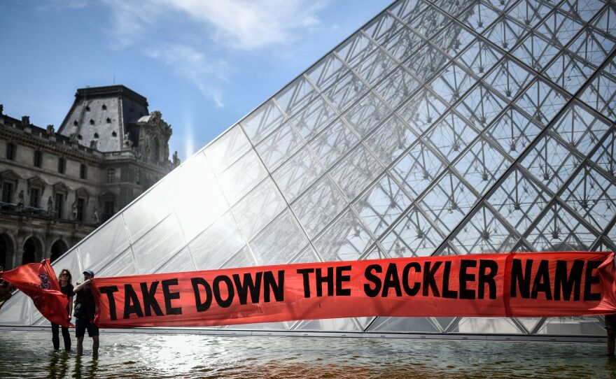 Activists raise a banner reading "Take down the Sackler name" during a demonstration earlier this year in front of the Louvre Pyramid in Paris.