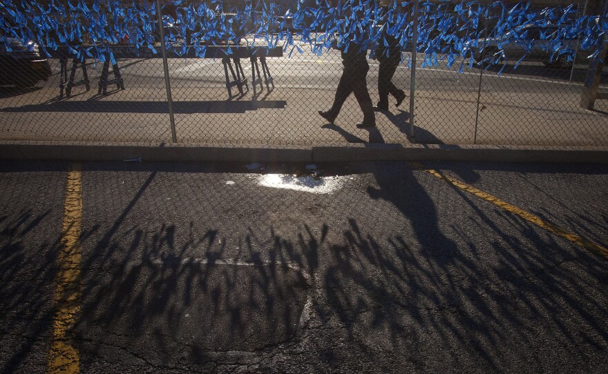 Police officers walk past a fence covered in blue ribbons as a makeshift tribute near Christ Tabernacle Church.