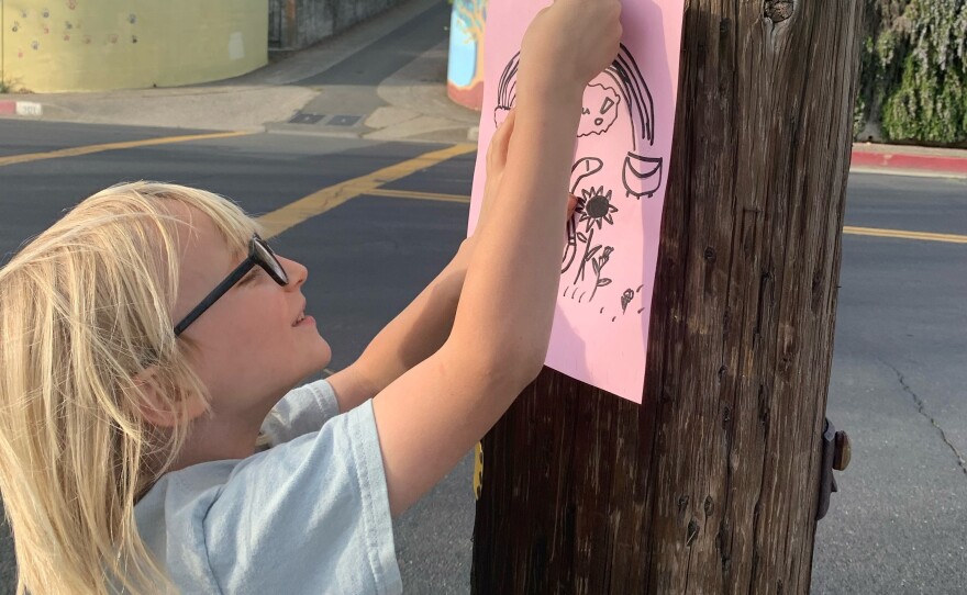 August Pochan, a West Side Elementary 1st grader, hangs a poster with encouraging words on a phone pole for the Peptoc project.
