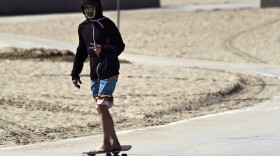 A skateboarder wears a face mask as he moves past Venice Beach, Monday, March 23, 2020, in Los Angeles. Venice Beach Boardwalk was officially closed Monday after widespread ignoring of social distancing over the weekend.

