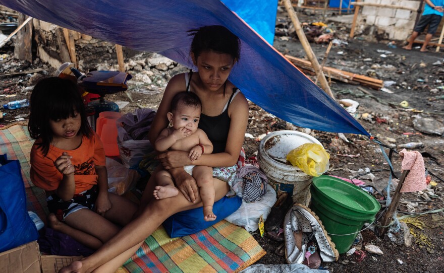 Joy Villanueva, 15, holds her baby. The slums where her family lived had burned down; they hope to build a new shack to replace the home they lost.