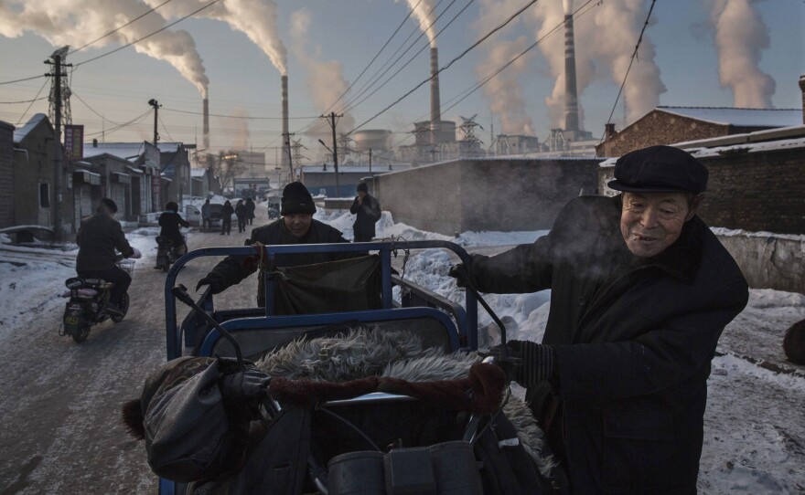 Men push a cart through a neighborhood in northern Shanxi, China as smoke billows from a coal-fired power plant in the distance.