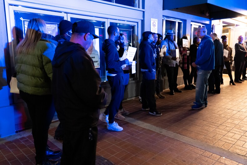 In the blue light of a nearby police vehicle, cannabis equity advocates protest Mayor Todd Gloria's annual state of the city address at Balboa Theatre on Wednesday, Jan. 10, 2024. Many of the advocates were arrested for cannabis crimes, and say they're effectively shut out of the now-legal industry.