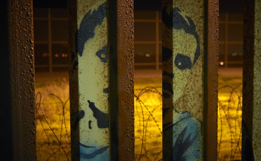 An image of a boy is painted on the bars of the border wall, in front of coils of razor wire, seen from Tijuana, Mexico. President Trump's proposal to end the partial government shutdown includes funding for more border wall, but also provisions that further restrict asylum seekers.