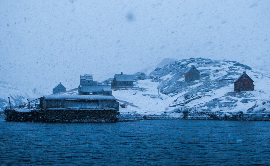 Kangeq's old wharf and houses appear ghostlike through a late winter snowstorm.