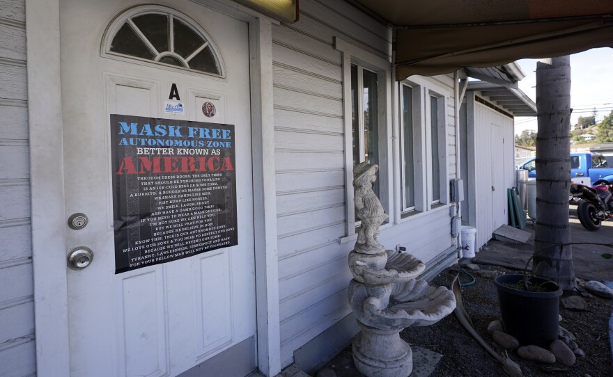 A sign against wearing masks to slow the spread of the coronavirus covers the office door of Fowler's Pool Services and Supply Inc, on Jan. 7, 2021, in Spring Valley, Calif. 