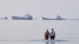 Two men wade in the waters of the Strait of Hormuz with vessels anchored in the background, off Bandar Abbas, Iran, Sunday, July 12, 2026.