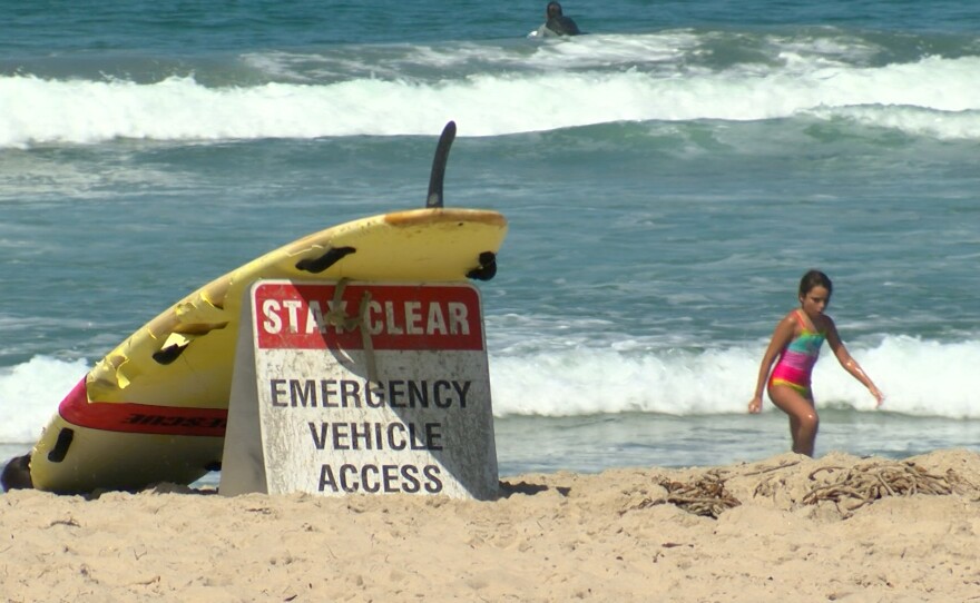 A surfboard leans against a "stay clear" sign on Mission Beach, CA on September 5, 2022.