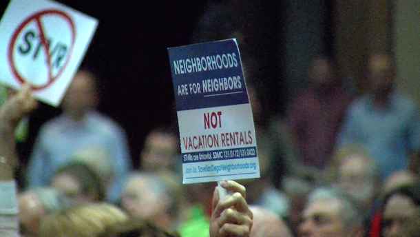 A hand holds up a sign reading "Neighborhoods are for neighbors, not vacation rentals" at a San Diego City Council meeting, Nov. 1, 2016.