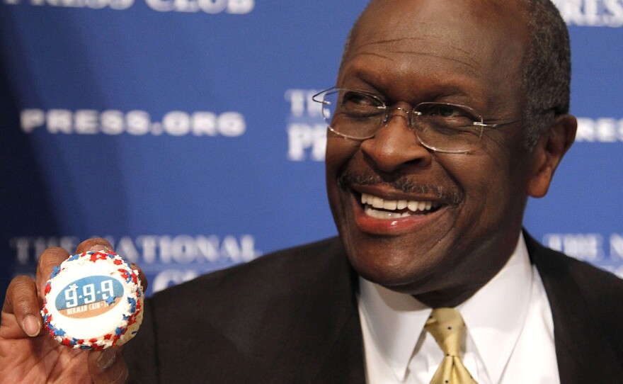 Herman Cain, then a GOP presidential candidate, holds a muffin bearing his catchphrase "9-9-9" tax plan at the National Press Club in Washington in 2011. Cain's death was announced Thursday.