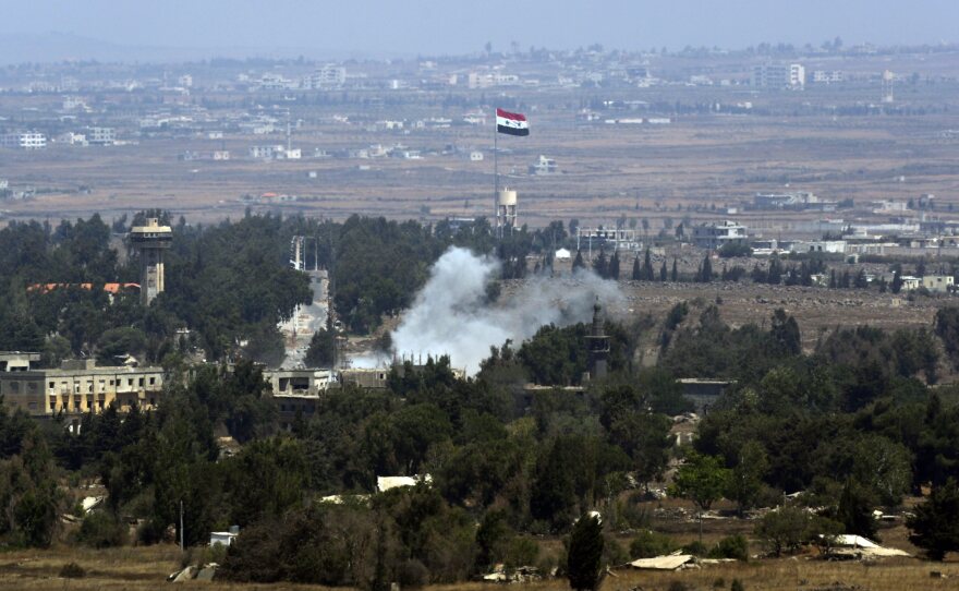 Smoke rises near a Syrian flag hoisted up a flagpole as a result of the fighting between Syrian rebels and the Syrian Army over the control of Quneitra crossing, on Saturday. The area is where  dozens of U.N. peacekeepers had been under siege by Nusra Front fighters.
