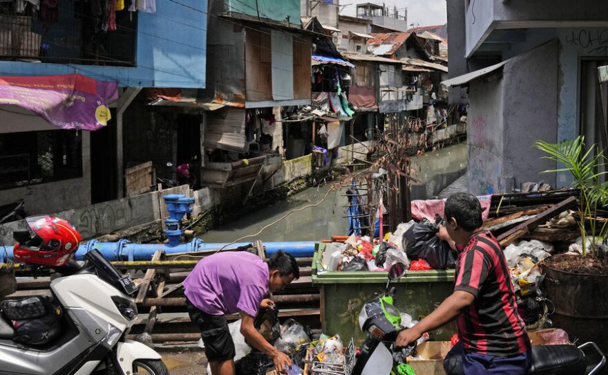Men put garbage bags into an open dumpster in a low-income neighborhood in Jakarta, Indonesia, Tuesday, Jan. 25, 2022.