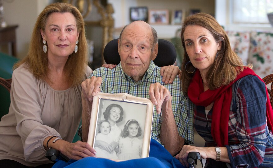 Laura Rees (left) and her sister Nancy Fee sit with their father, Joseph Fee, while holding a photo of his late wife, Elizabeth.