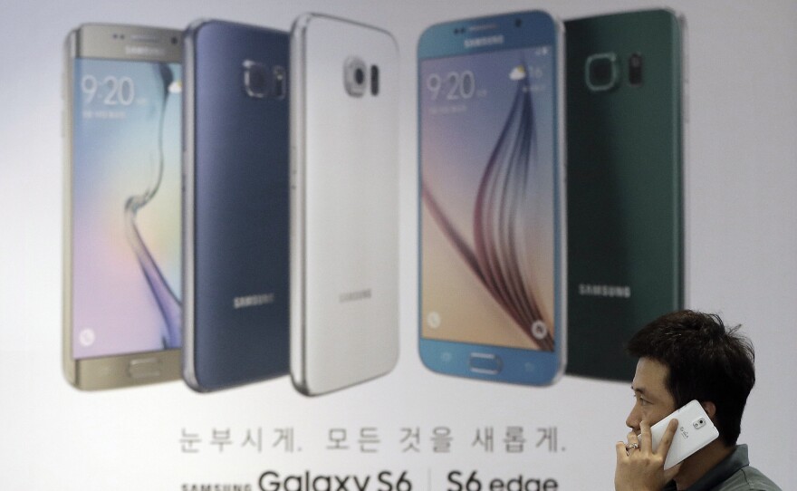 A visitor uses his smartphone in front of an advertisement of Samsung Electronics' Galaxy S6 and S6 Edge smartphone at a Samsung Electronics shop in Seoul, South Korea, in 2015.