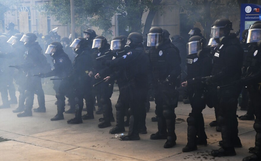 Officers in Aurora, Colo., face off with protesters over Elijah McClain's death outside police headquarters Saturday at the Aurora Municipal Center. The department says it's investigating photos that officers took at a memorial site for McClain, who died in police custody in 2019.