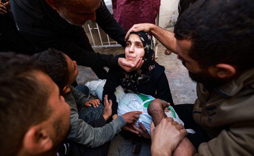 People try to comfort a woman holding the body of her baby girl killed in an Israeli strike in Rafah, southern Gaza Strip, in the courtyard of the al-Najjar hospital on Dec. 1, after battles resumed between Israel and Hamas.