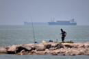 A man stands beside a fishing pole along the shore as cargo ships and commercial vessels are seen in the Strait of Hormuz off Bandar Abbas, Iran, Wednesday, June 17, 2026.