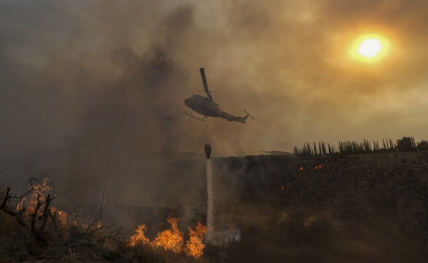A helicopter drops water on the Fairview Fire burning on a hillside Thursday, Sept. 8, 2022, near Hemet, Calif. Scientists say a warming planet will lead to hotter, longer and more wildfire-plagued heat waves.